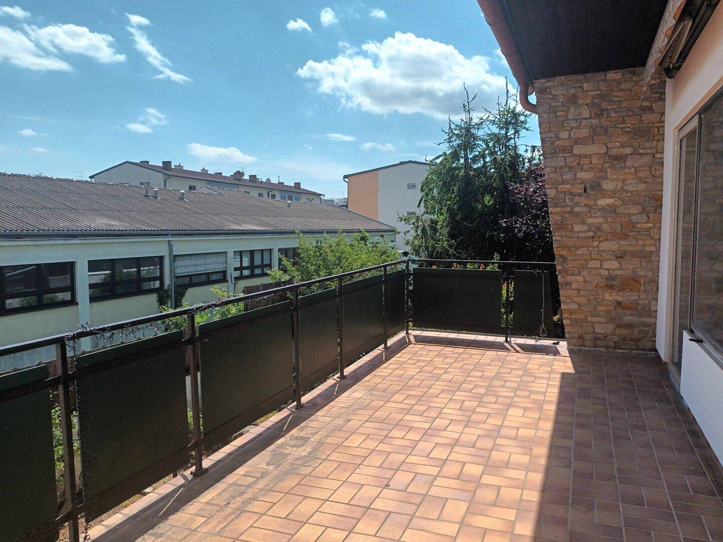 Großer Balkon mit Fliesenboden und Blick auf die umliegenden Gebäude und Bäume.