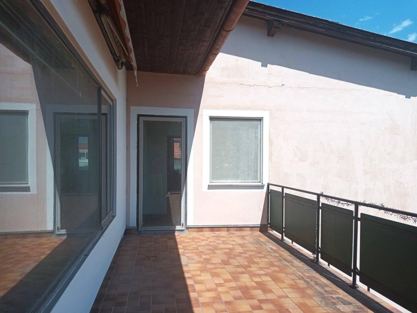 Geräumiger Balkon mit Fliesenboden und Zugang zu einem Innenraum des Hauses.