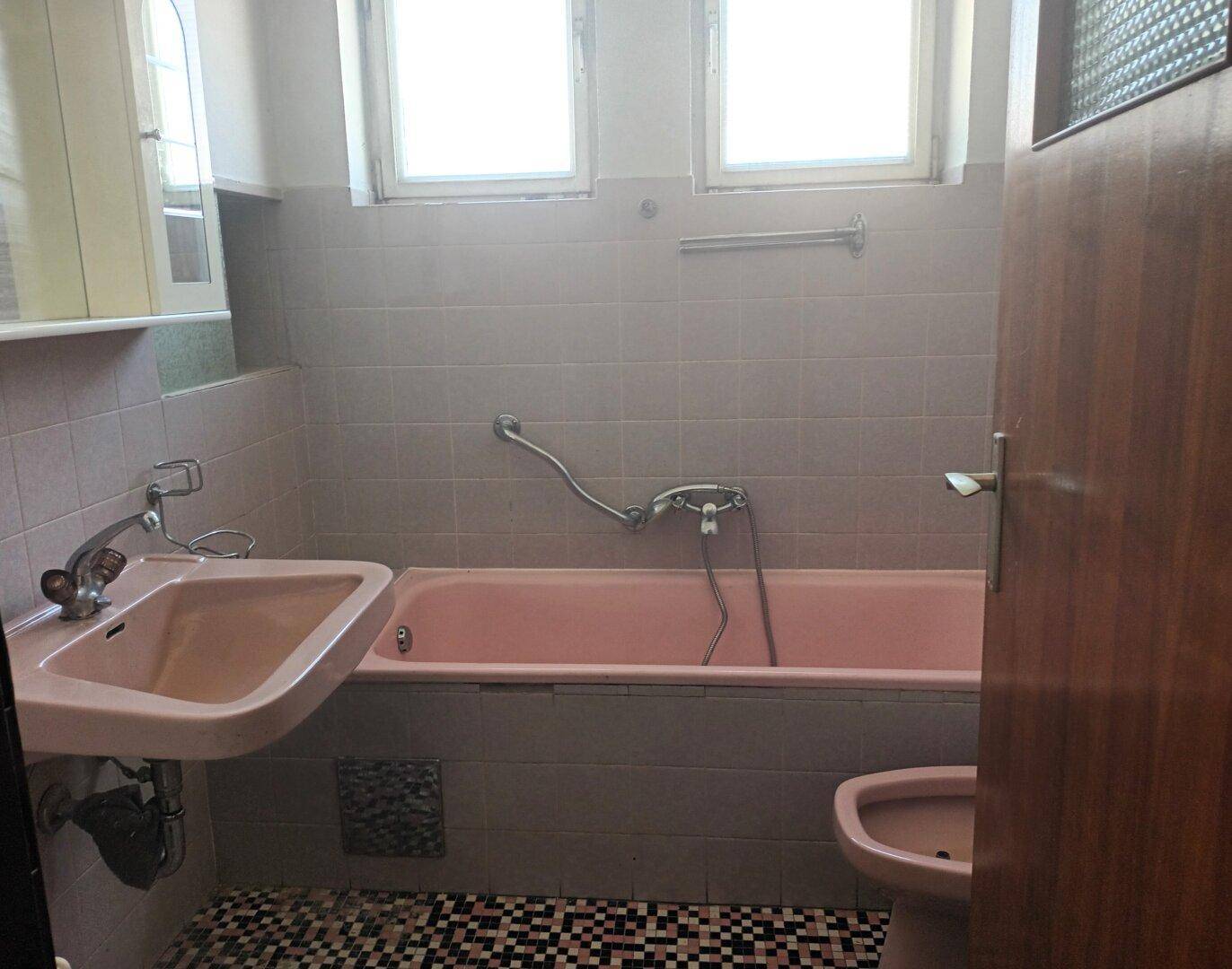 Badezimmer im 80er-Jahre-Stil mit rosa Badewanne, Waschbecken und Fliesen.