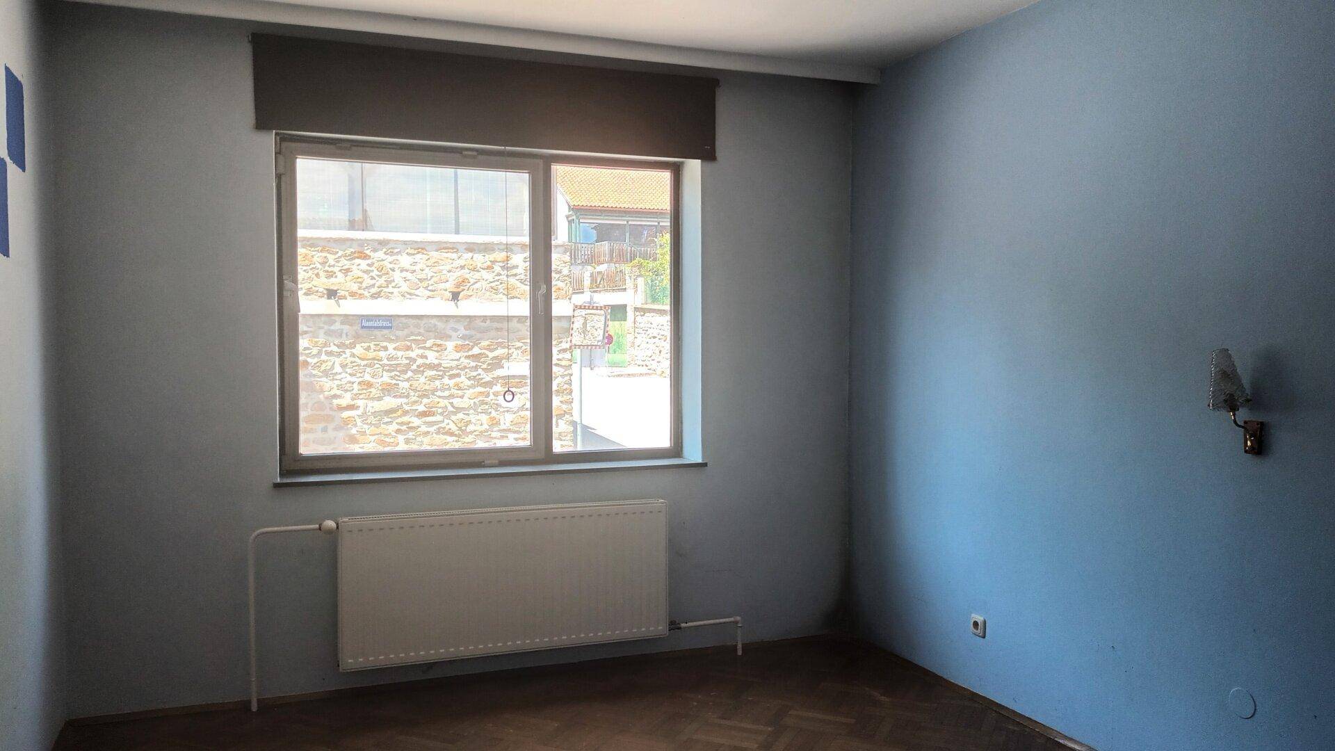 Schlafzimmer mit blauen Wänden, Parkettboden und Fenster mit Blick auf die Umgebung.