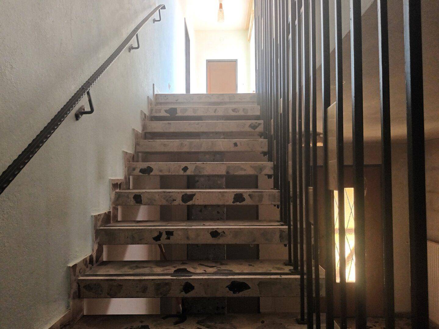 Treppenhaus mit Steinstufen und Metallgeländer, das in die oberen Stockwerke führt.