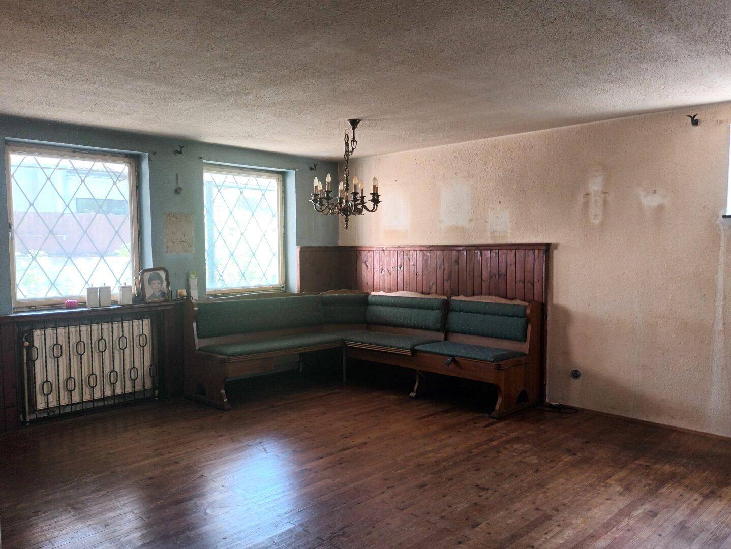 Wohnzimmer mit Holzboden, eingebauter Sitzbank und Fenstern mit Gittermuster.