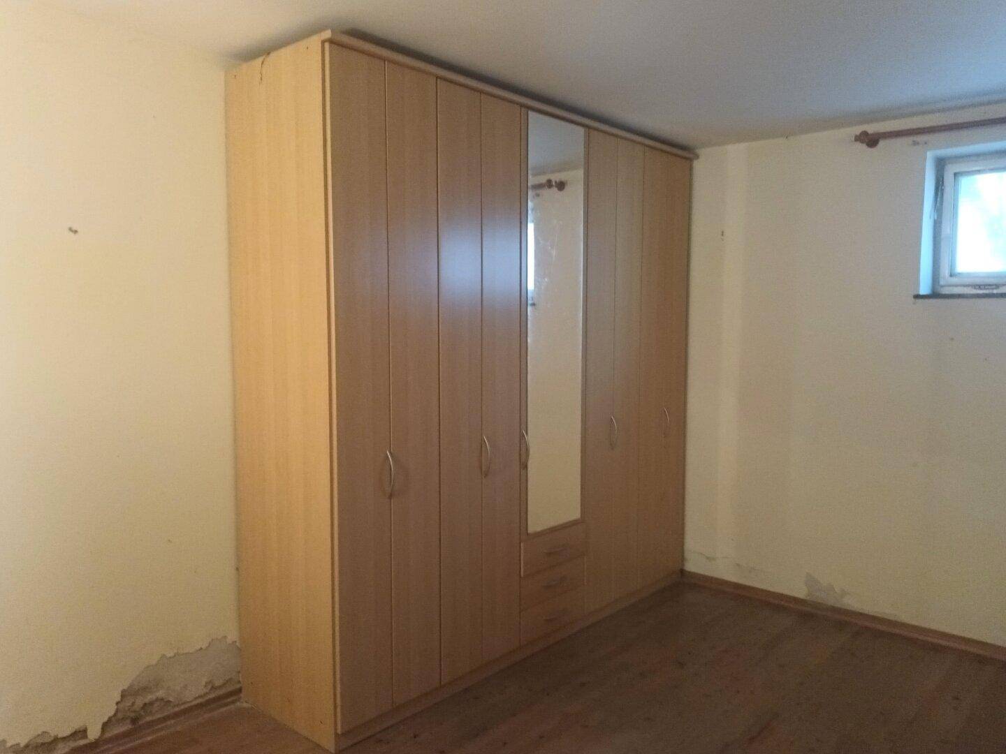Schlafzimmer mit großem Kleiderschrank, Holzfußboden und kleinem Fenster.