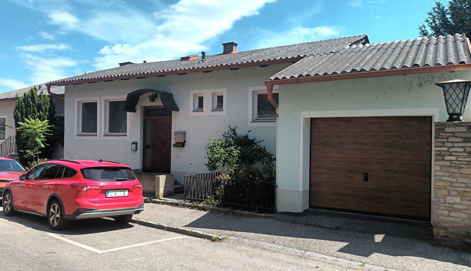 Vorderansicht des Hauses von der Straße aus mit geparkten Autos und Garagentor.