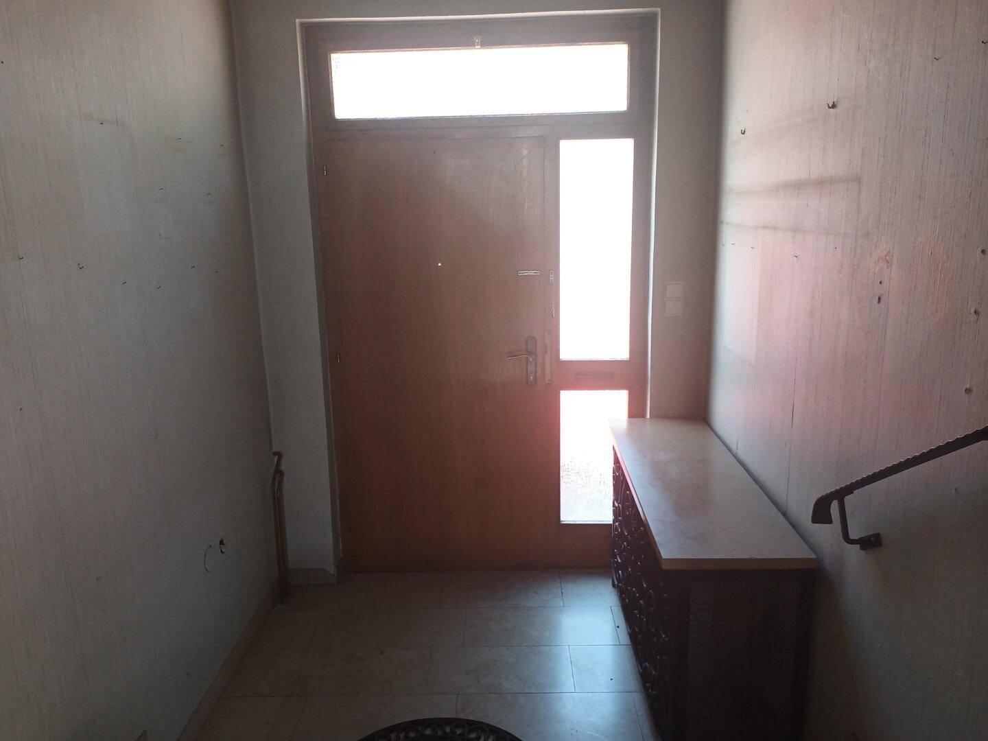 Eingangsbereich mit Fliesenboden, Holztür und einem kleinen Schrank.