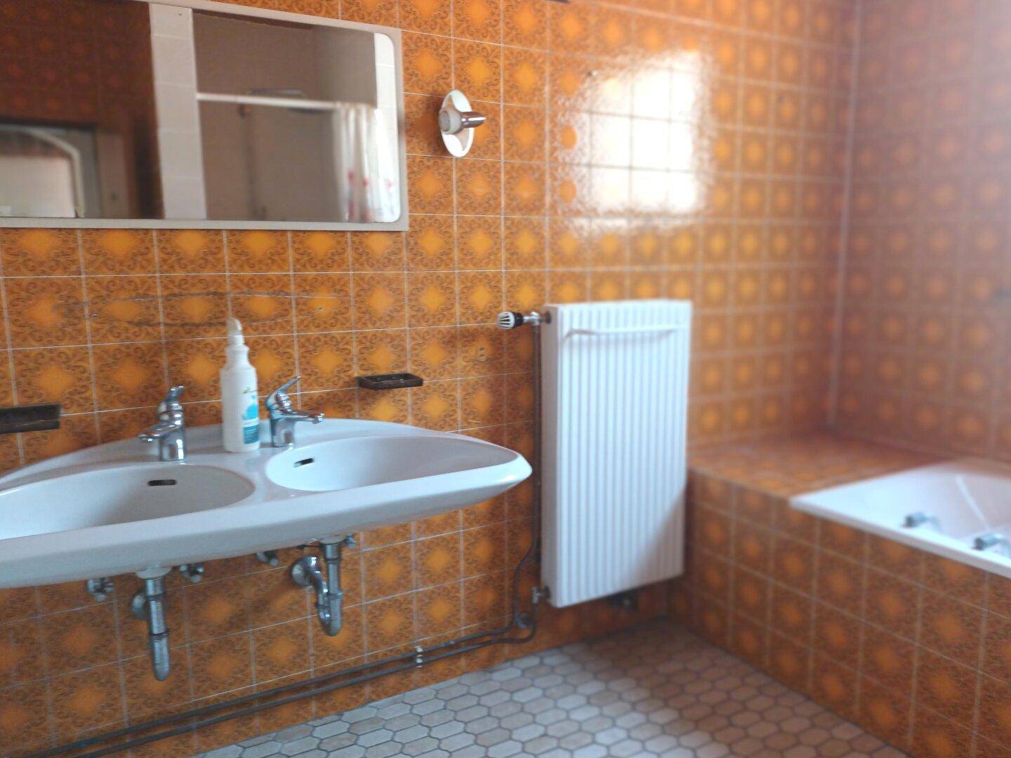 Badezimmer mit orangefarbenen Fliesen, Doppelwaschbecken und einer Badewanne.