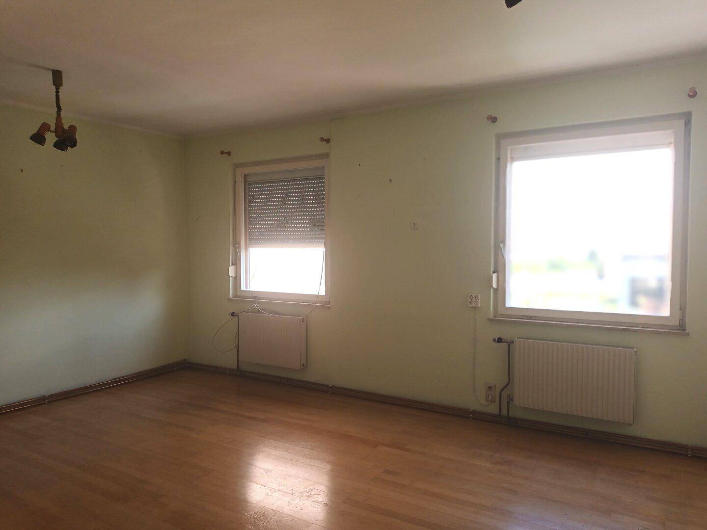 Geräumiges Zimmer mit Holzfußboden, zwei Fenstern und Heizkörpern.