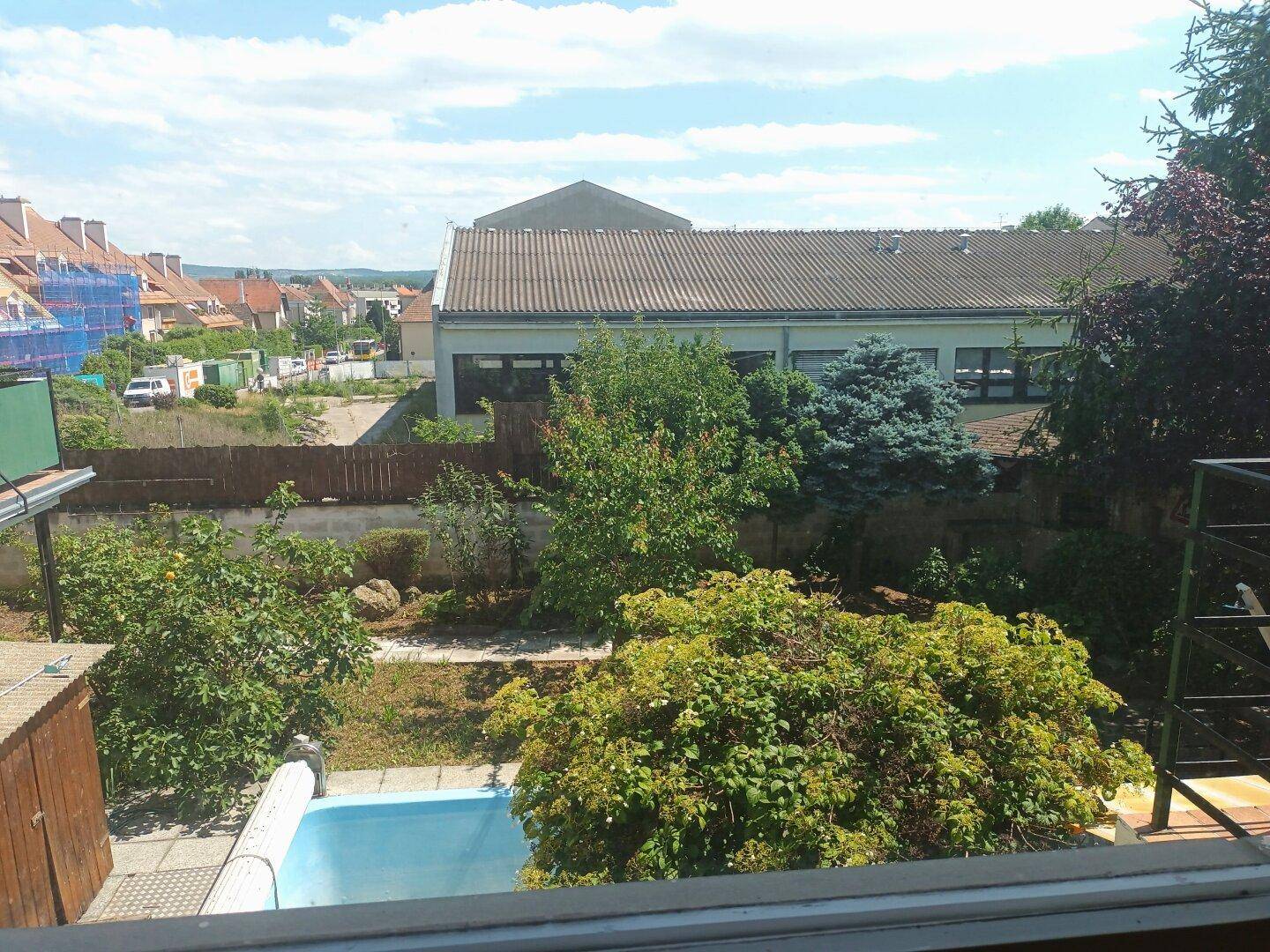 Blick aus dem Fenster auf einen Garten mit kleinem Pool und umliegende Häuser.