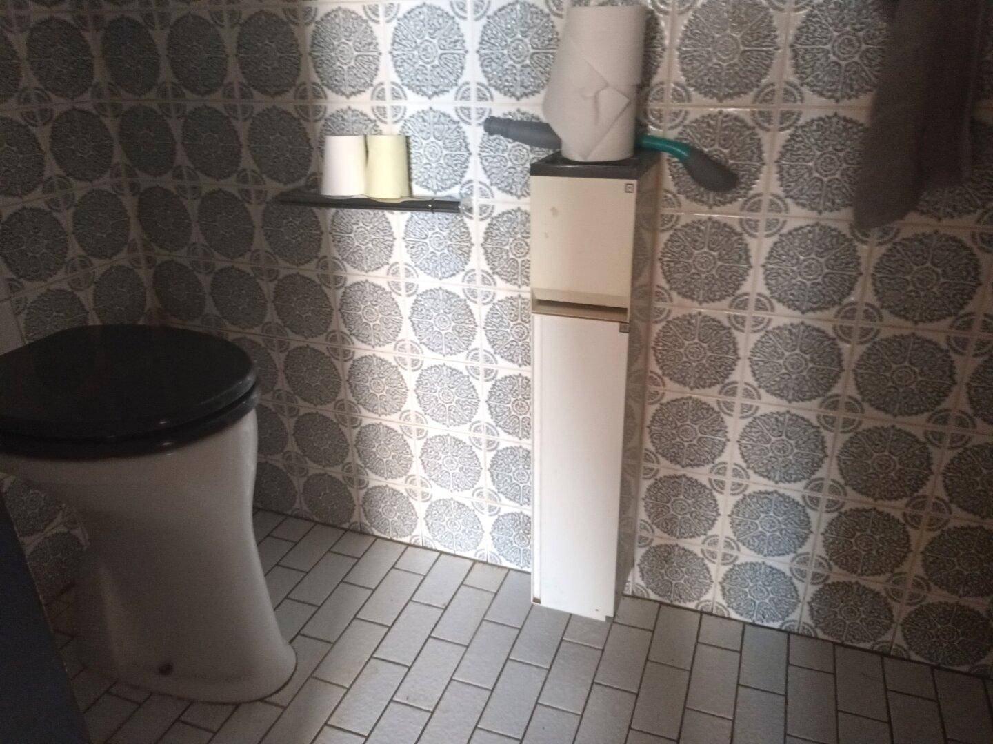Toilette mit grauen gemusterten Fliesen und einem schwarzen Toilettensitz.