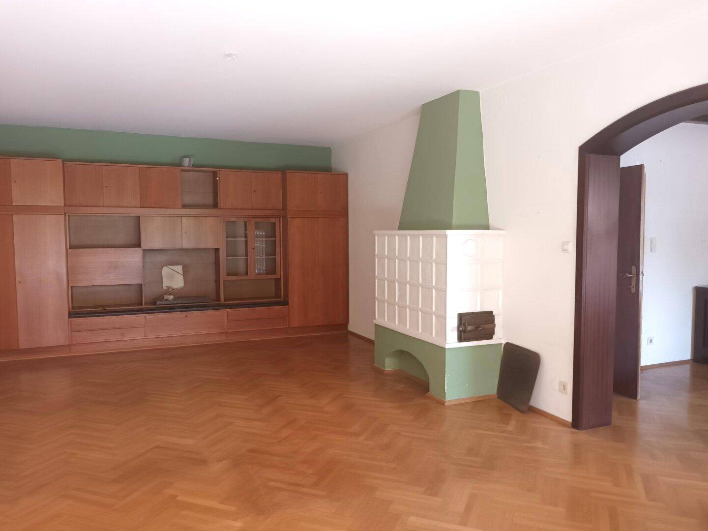 Wohnzimmer mit Parkettboden, Einbauschrank und einem traditionellen Kachelofen.