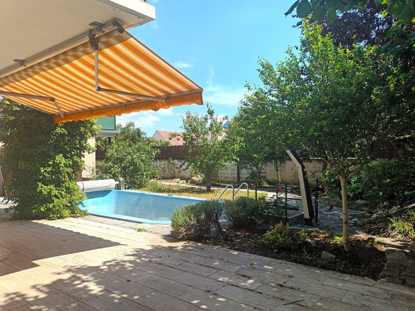 Außenbereich mit Terrasse, Pool, Markise und üppiger Bepflanzung.