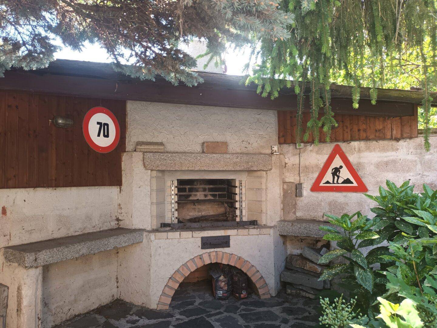 Gemütlicher Grillbereich im Freien mit eingebautem Grill und Sitzgelegenheiten aus Stein.