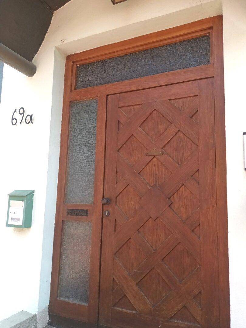 Detailansicht der verzierten Holzeingangstür mit Hausnummer 69a und Briefkasten.