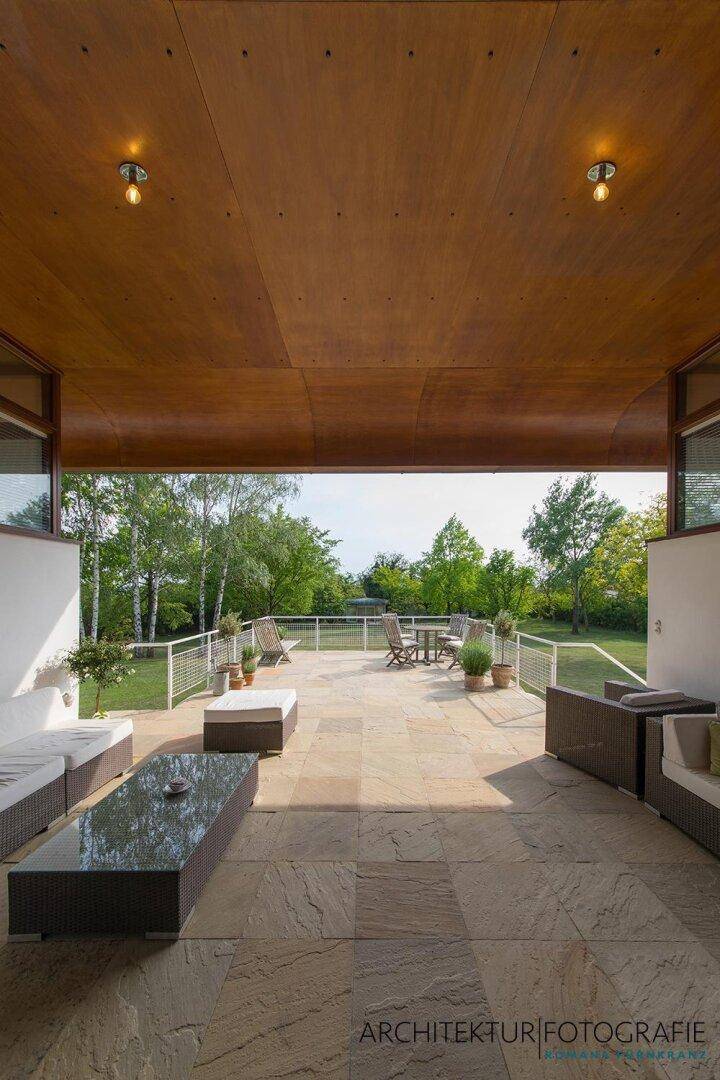 Große überdachte Terrasse mit Sitzgelegenheiten und weitem Blick in den Garten.