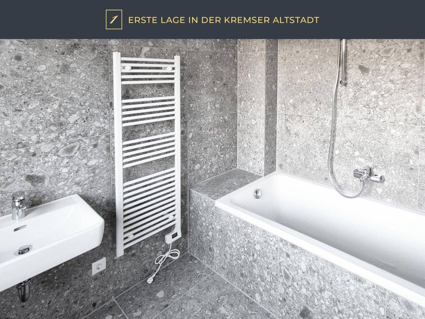 Modernes Badezimmer mit Badewanne, kleinem Waschbecken und beheiztem Handtuchhalter.