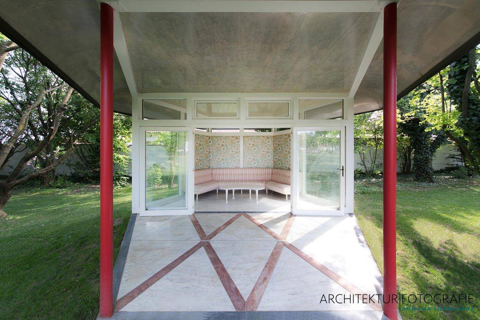 Einladender Gartenpavillon mit floraler Tapete, bequemen Sitzgelegenheiten und gemustertem Boden.