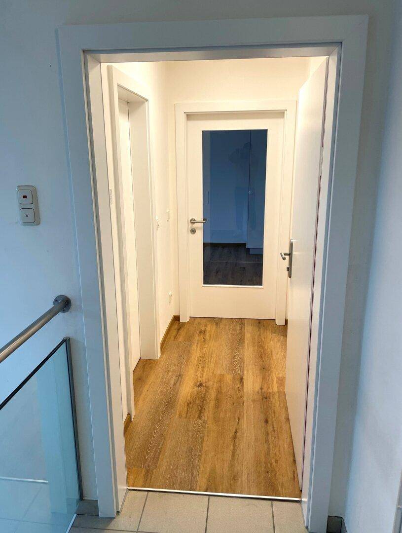 Heller Flur mit Holzboden und weißen Türen, der zu weiteren Räumen führt.