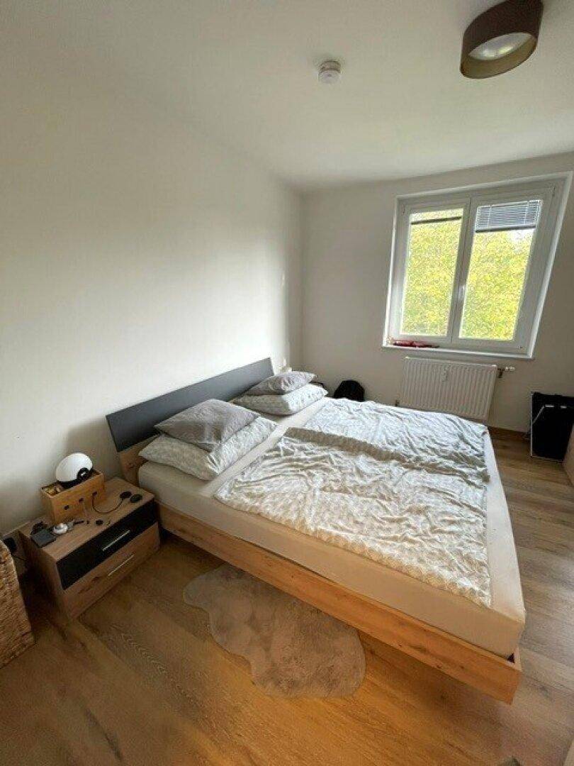 Gemütliches Schlafzimmer mit Doppelbett, Nachttischen und einem Fenster, das viel Tageslicht hereinlässt.