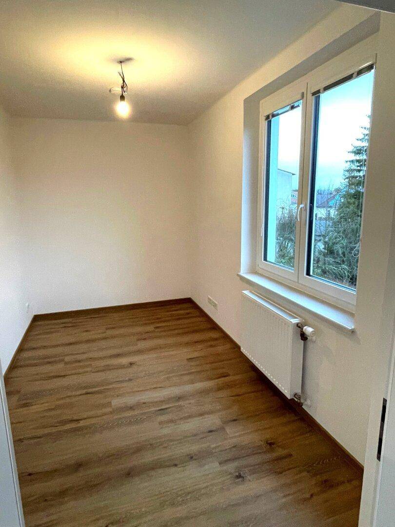 Leeres Zimmer mit Holzboden und einem großen Fenster, das für viel Helligkeit sorgt.