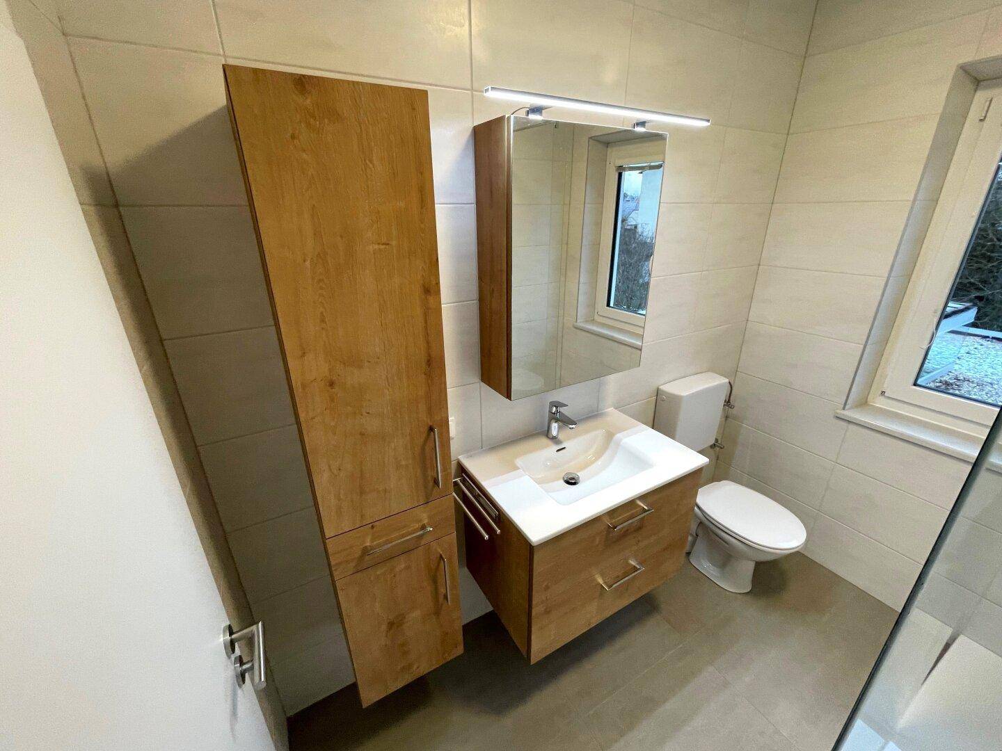 Modernes Badezimmer mit Holzwaschtisch, Spiegelschrank, WC und hellen Fliesen an Wänden und Boden.
