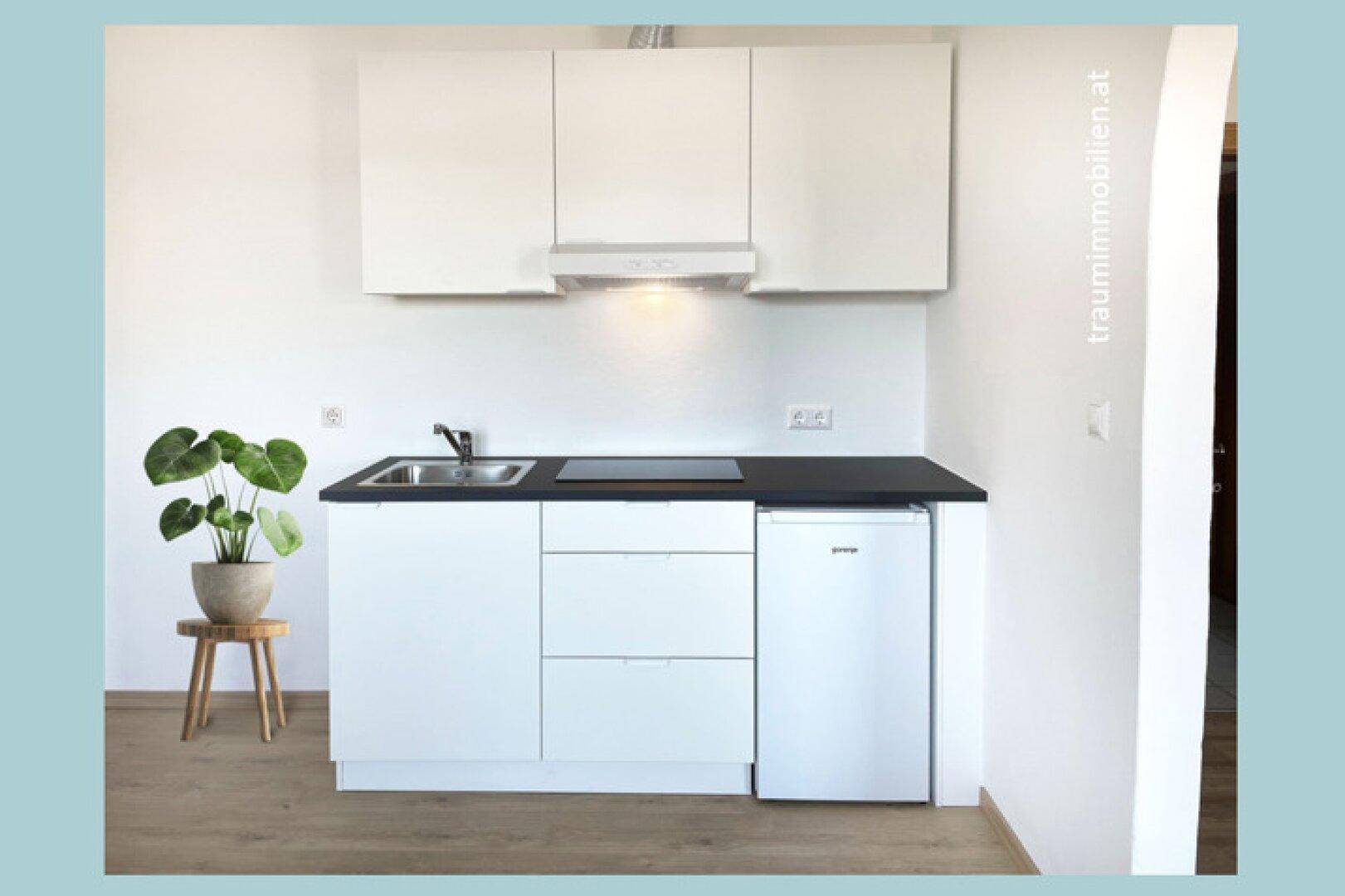 Kleine, moderne Küchenzeile mit weißen Schränken, schwarzer Arbeitsplatte und integriertem Kühlschrank.
