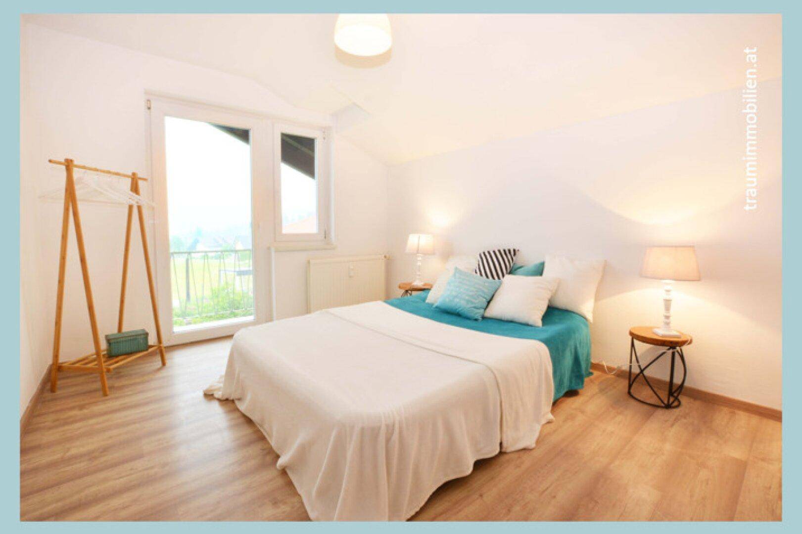 Gemütliches Schlafzimmer mit Doppelbett, Laminatboden und Zugang zu einem Balkon oder einer Terrasse.