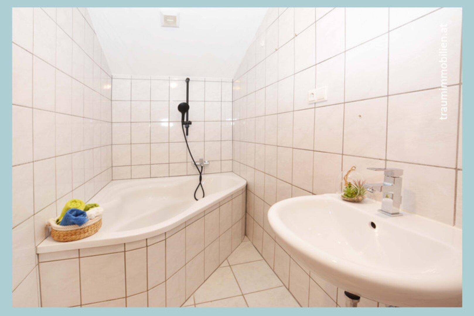 Badezimmer mit weißen Fliesen, einer Eckbadewanne und einem einzelnen Waschbecken.