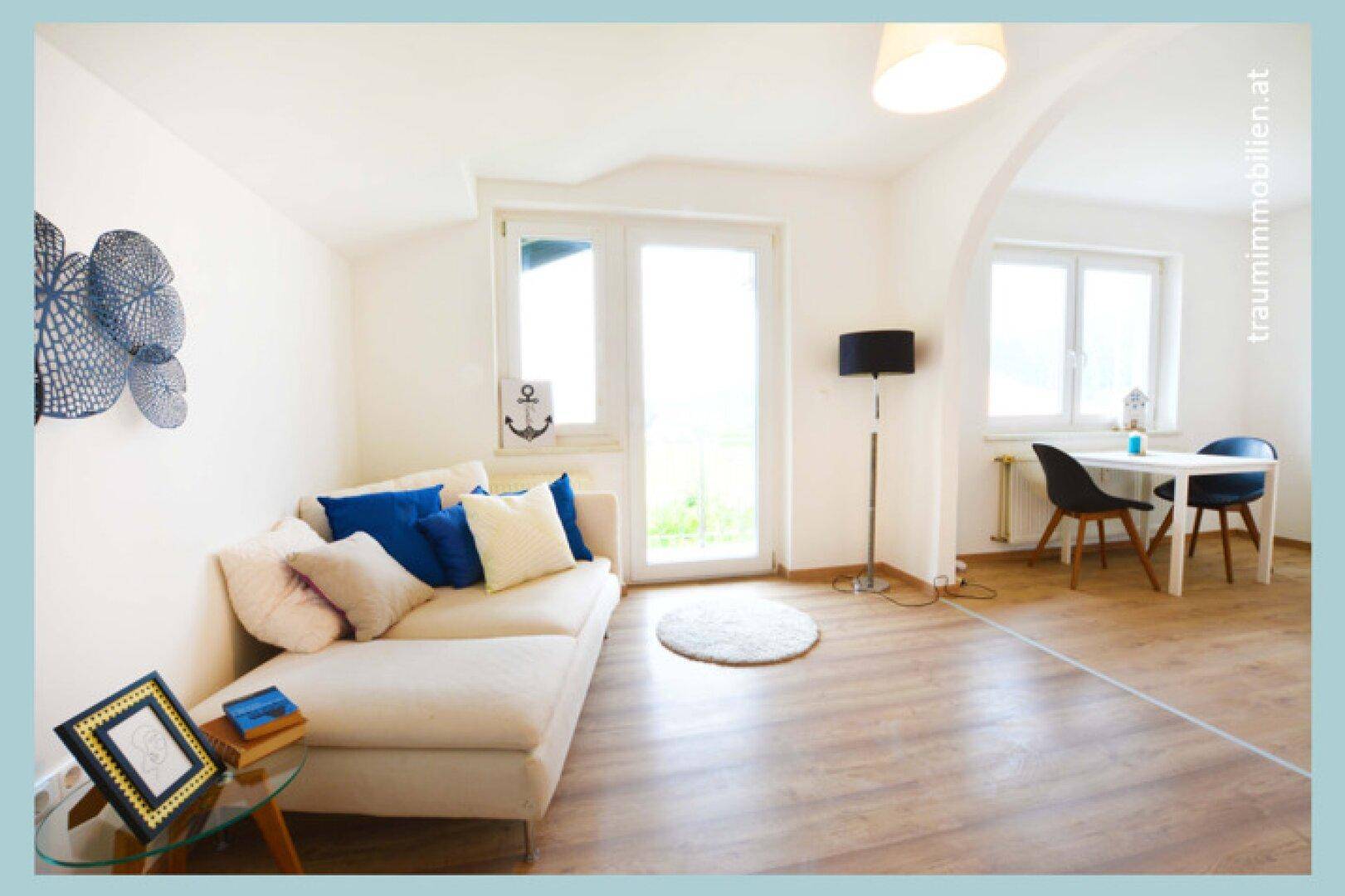 Helles Wohnzimmer mit Sofa, Laminatboden und Zugang zu einem Außenbereich.