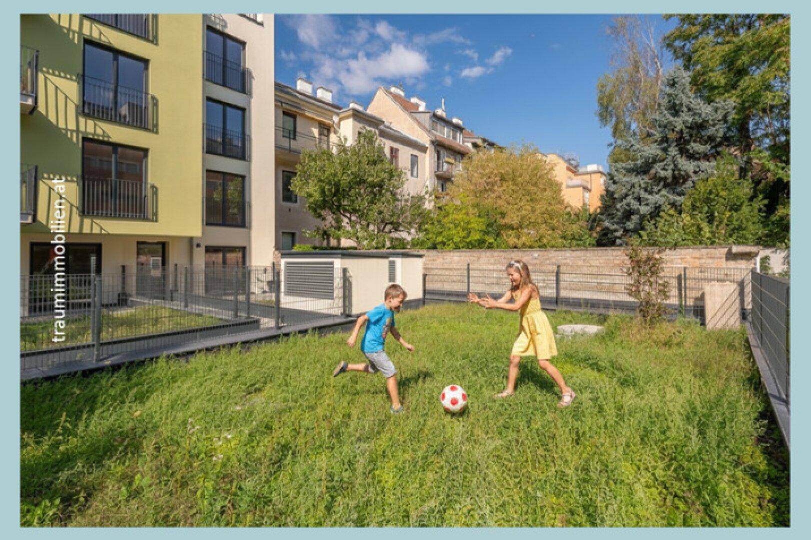 Kinder spielen Fußball auf der Rasenfläche vor dem modernen Wohngebäude.