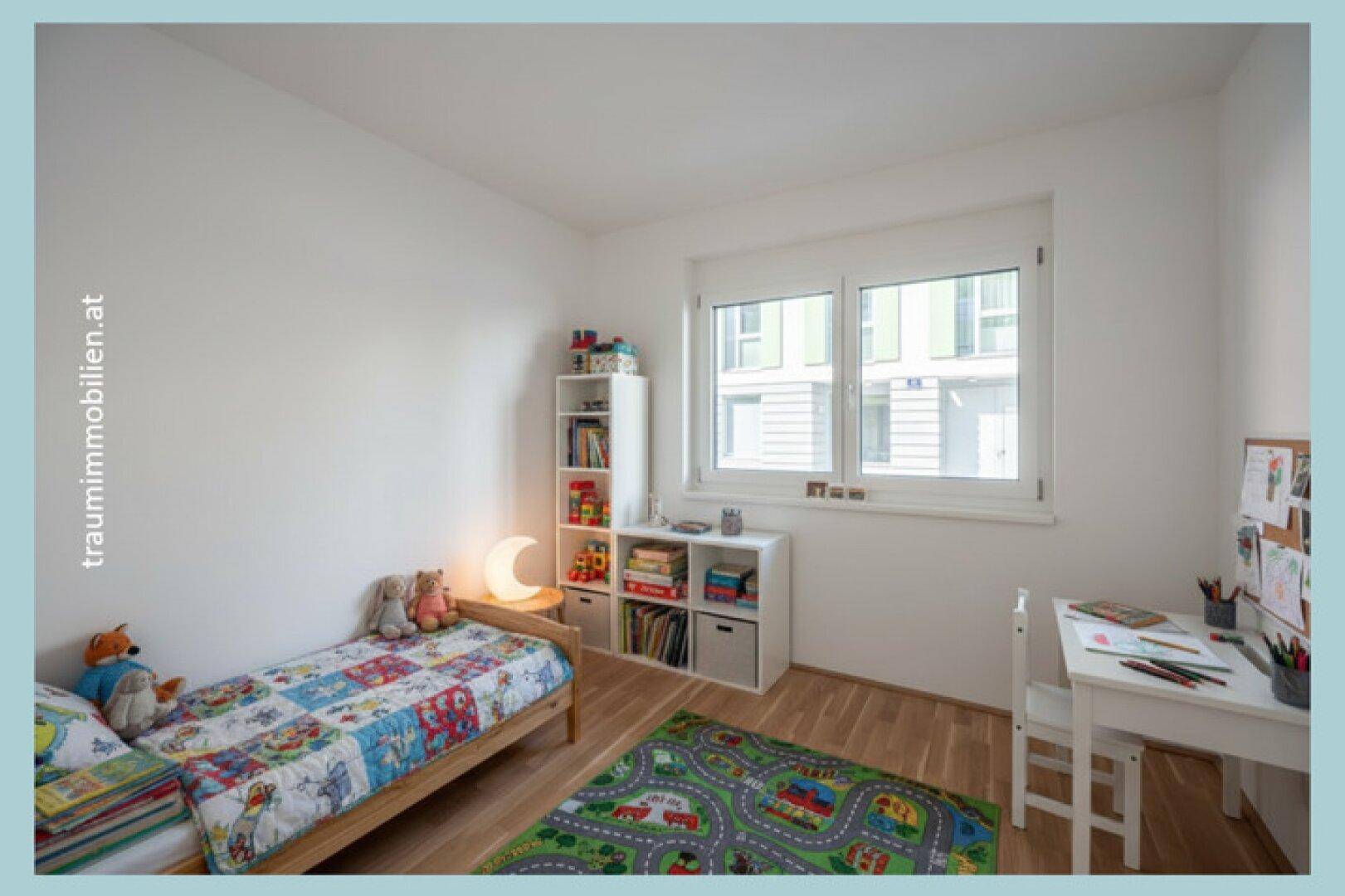 Helles Kinderzimmer mit Bett, Schreibtisch und Spielzeugregalen.