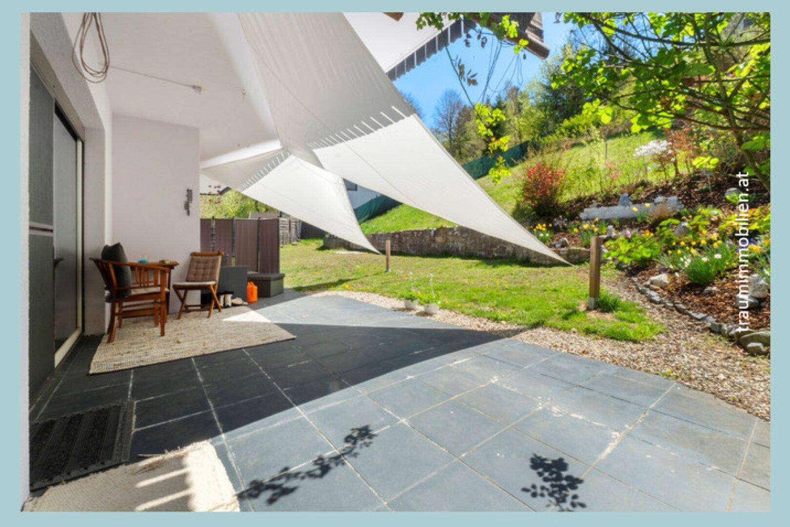 Geflieste Terrasse mit Outdoor-Sitzbereich, Sonnensegel und Zugang zum grünen Garten.