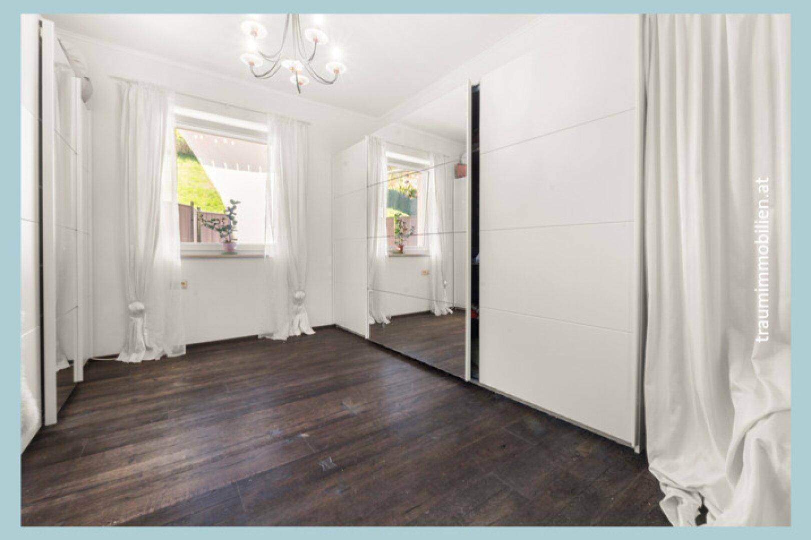 Heller Raum mit dunklem Holzboden, weißen Wänden und großem Spiegelschrank.