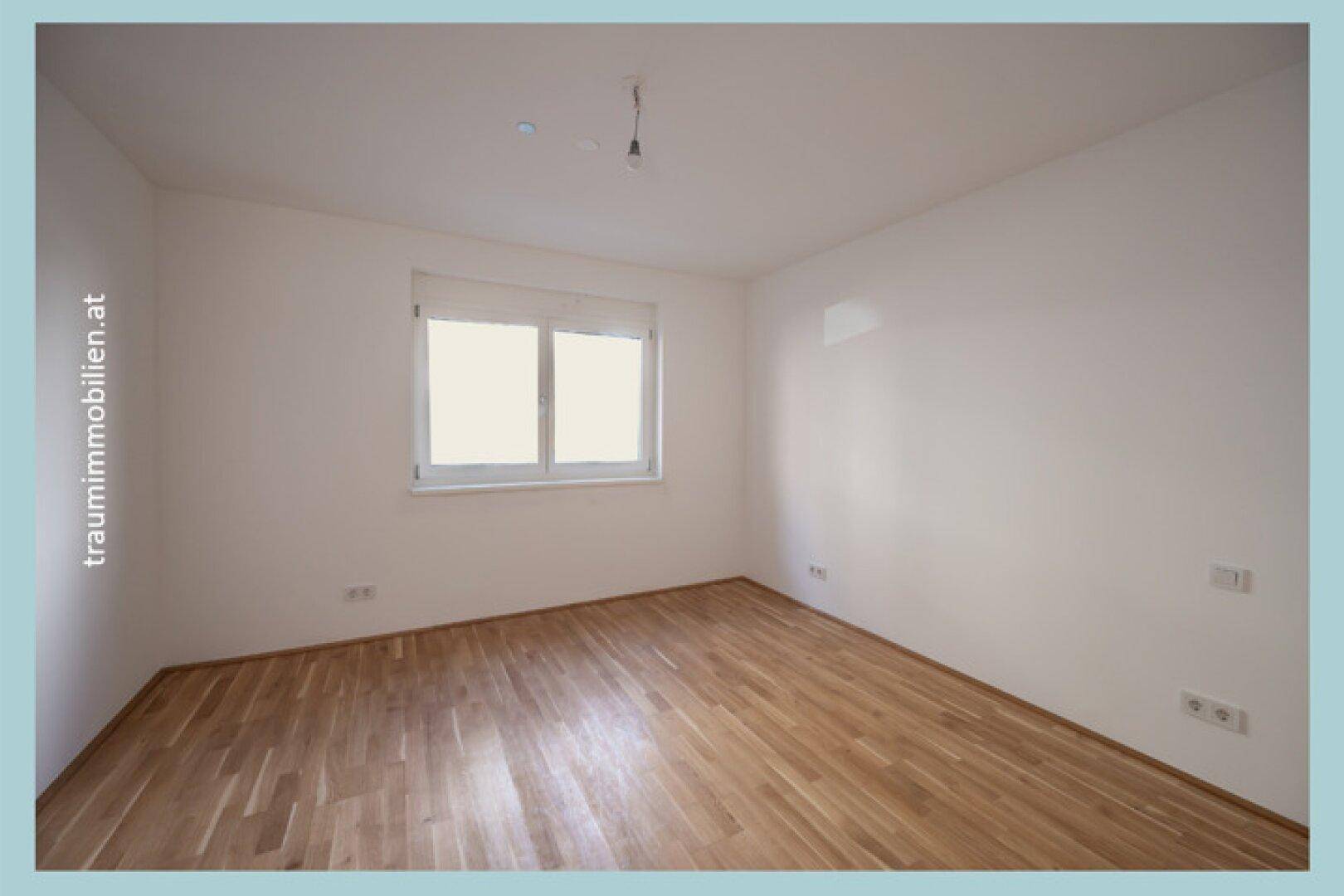 Helles Schlafzimmer mit Parkettboden und großem Fenster zum Garten.