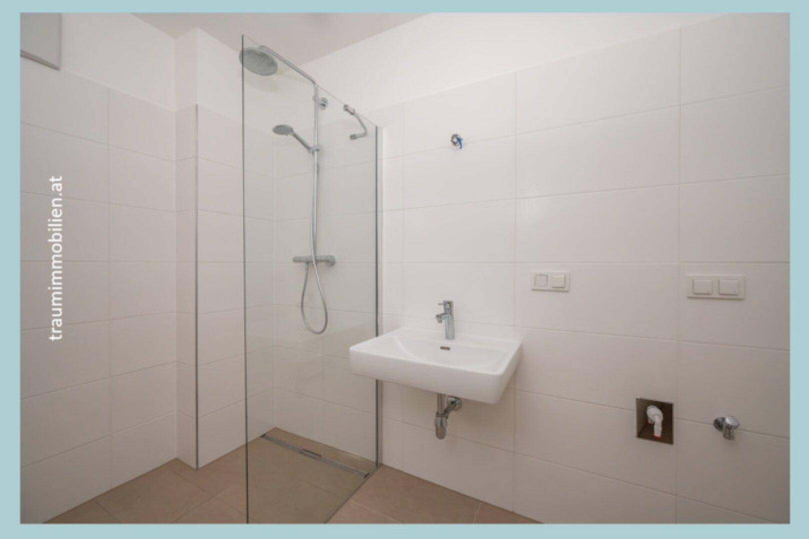 Modernes Badezimmer mit ebenerdiger Dusche, weißen Fliesen und Einzelwaschbecken.