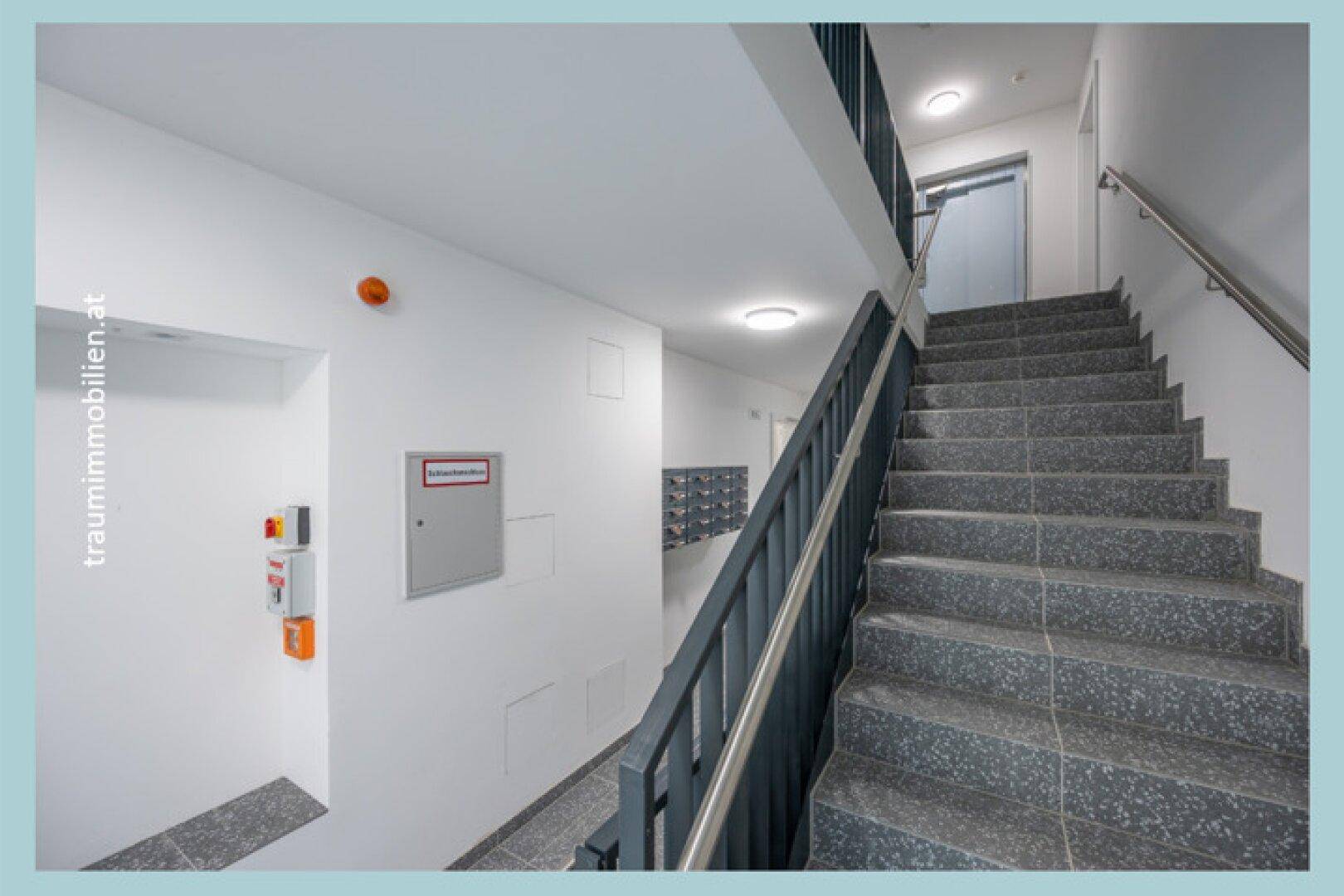 Helles Treppenhaus mit Granitstufen und Handlauf in einem modernen Gebäude.