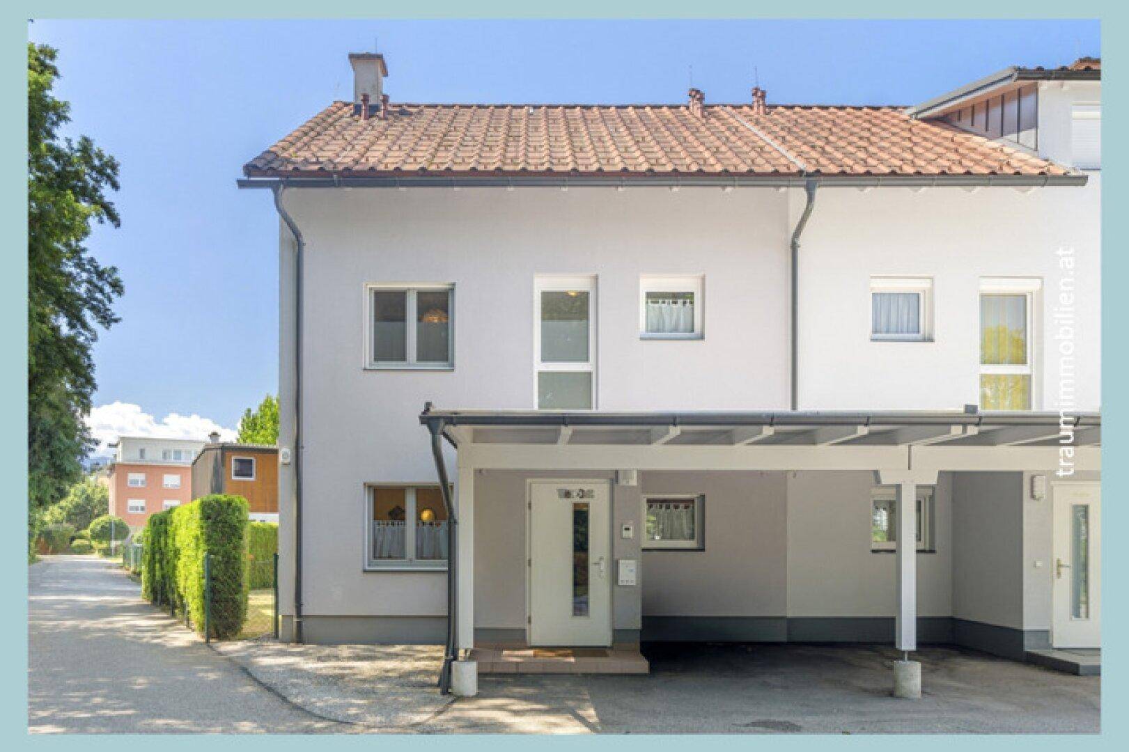 Moderne Hausfassade mit weißem Putz, Ziegeldach und überdachtem Carport am Eingangsbereich.