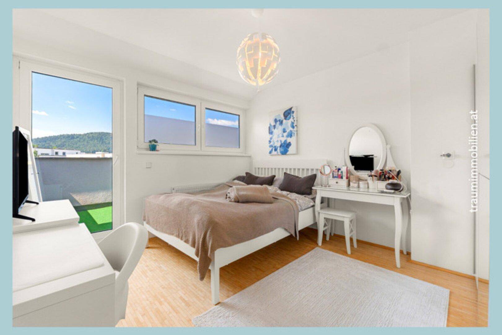 Helles Schlafzimmer mit Holzboden, modernem Bett, Schreibtisch und Zugang zu einem kleinen Balkon.