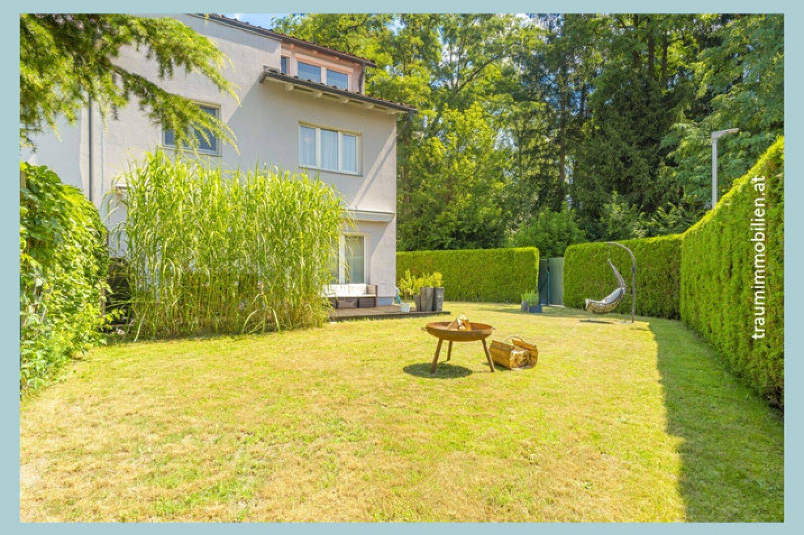 Gepflegter Garten mit Rasenfläche, hohen Gräsern, Hecke und einer Feuerstelle für gemütliche Abende.