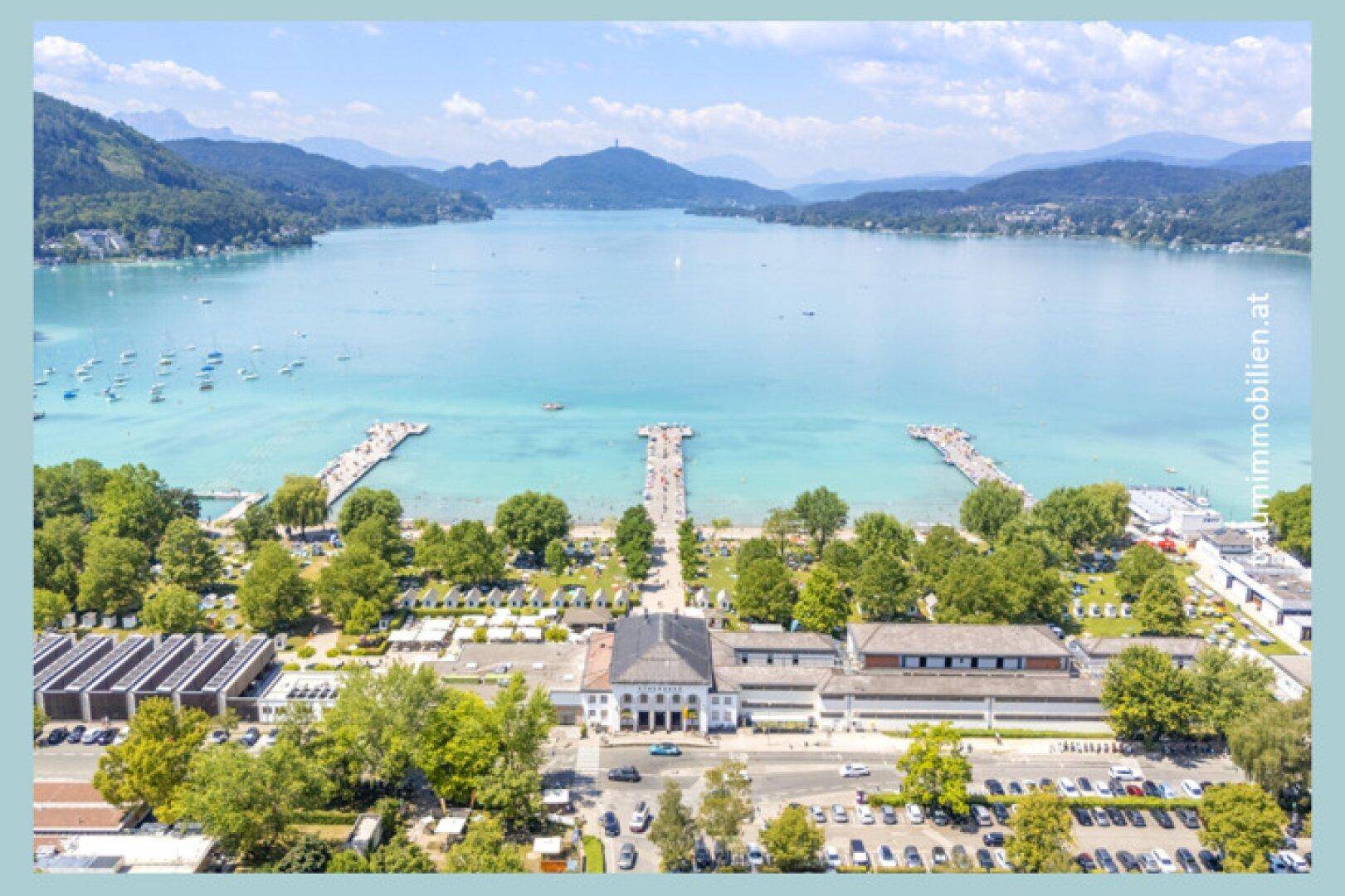 Panoramablick auf den Wörthersee mit Bergen im Hintergrund und einer belebten Uferpromenade.