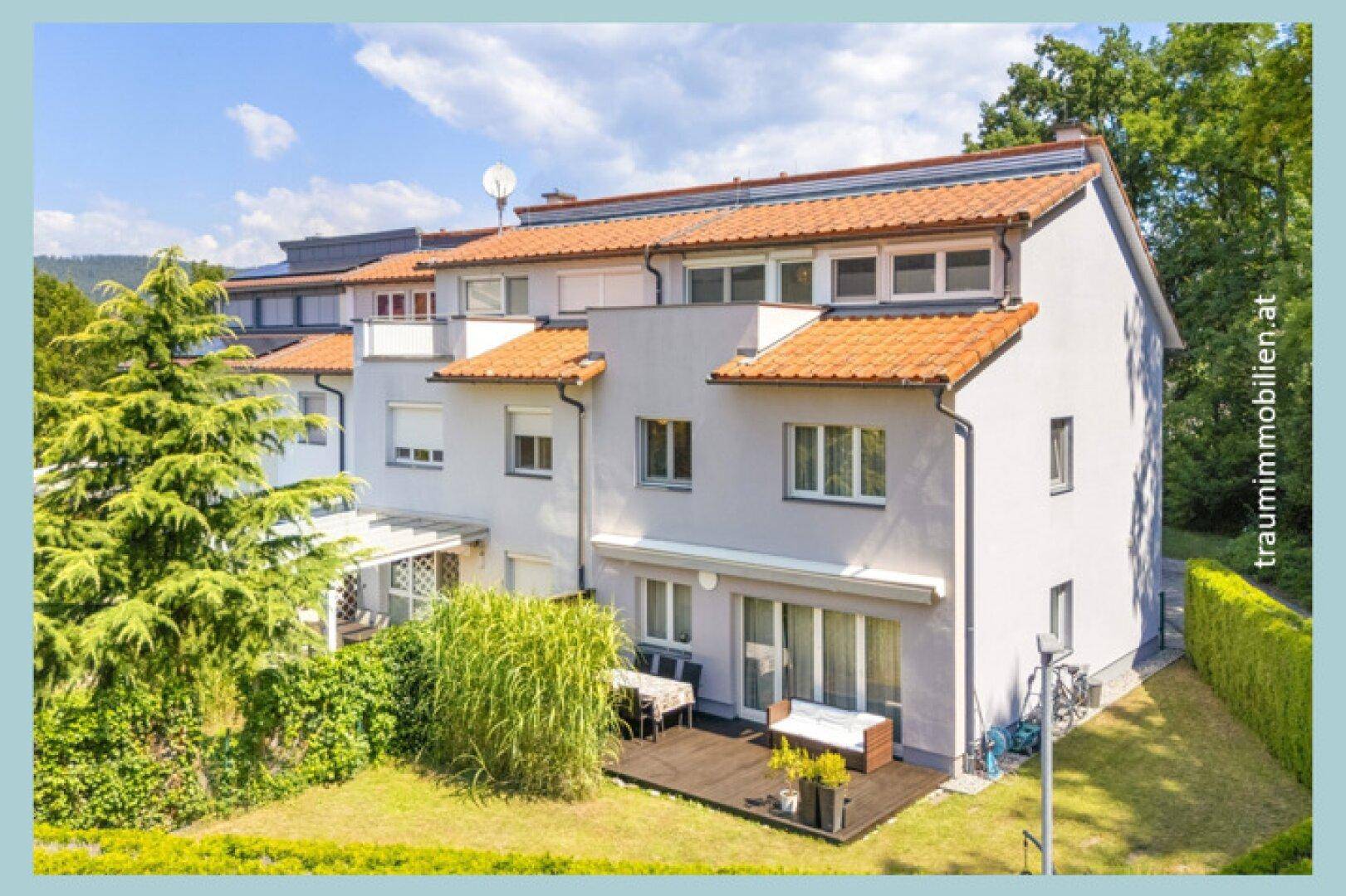 Rückansicht der Häuser mit privaten Gärten, Holzterrassen und üppiger grüner Bepflanzung.