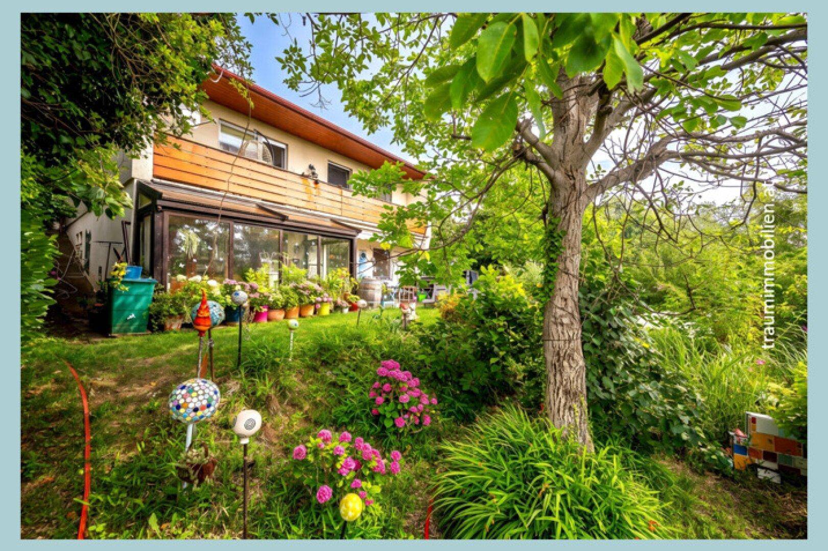 Ein charmantes Haus mit Wintergarten, eingebettet in einen üppigen, terrassierten Garten mit dekorativen Elementen und alten Bäumen.