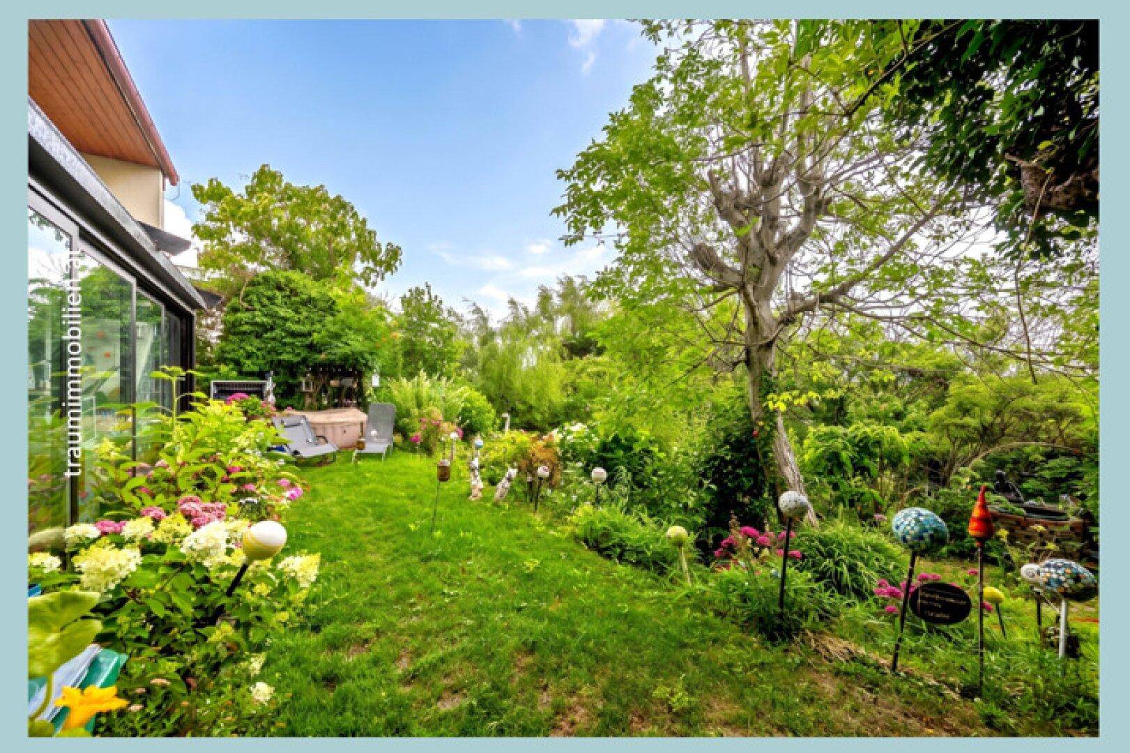 Ein weitläufiger, gepflegter Garten mit Rasenfläche, bunten Blumenbeeten und dekorativen Kugeln, der zum Haus führt.