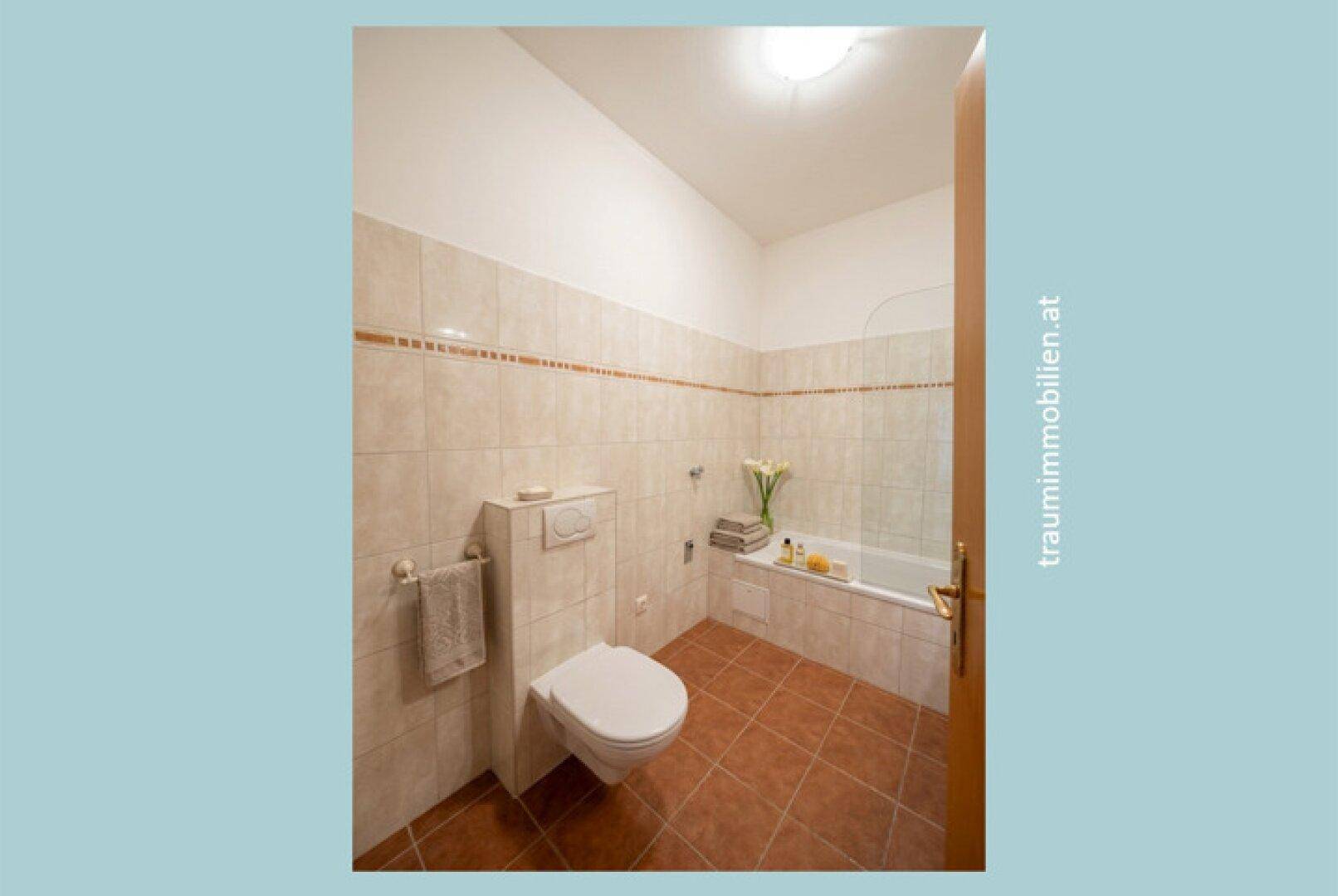 Badezimmer mit beigefarbenen Fliesen, Toilette und Badewanne.