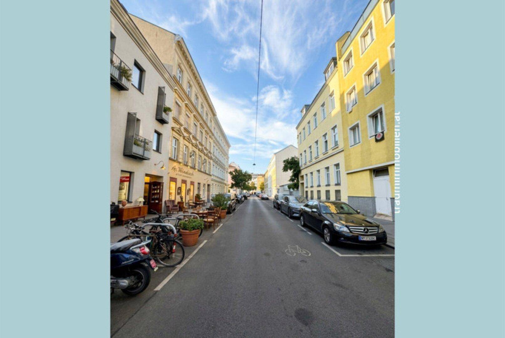 Ruhige Wohnstraße mit geparkten Autos und historischen Gebäuden in der Umgebung.