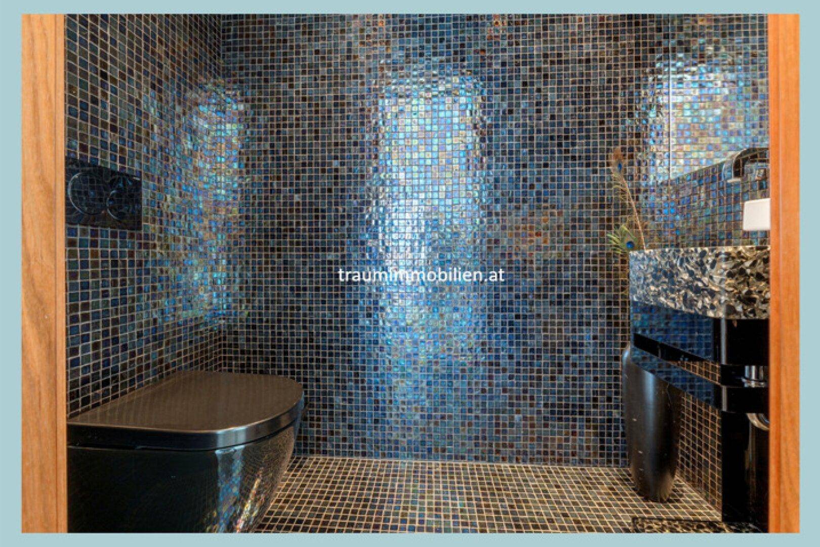 Exklusives Gäste-WC mit glänzenden Mosaikfliesen, schwarzer Toilette und modernem Waschbecken.