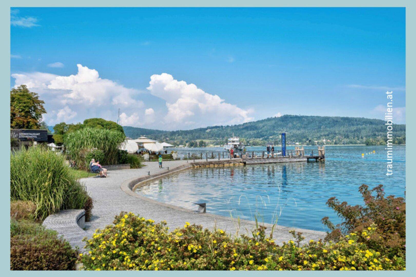 Lebhafte Seepromenade mit Sitzgelegenheiten, Grünflächen und einem Bootsanleger.