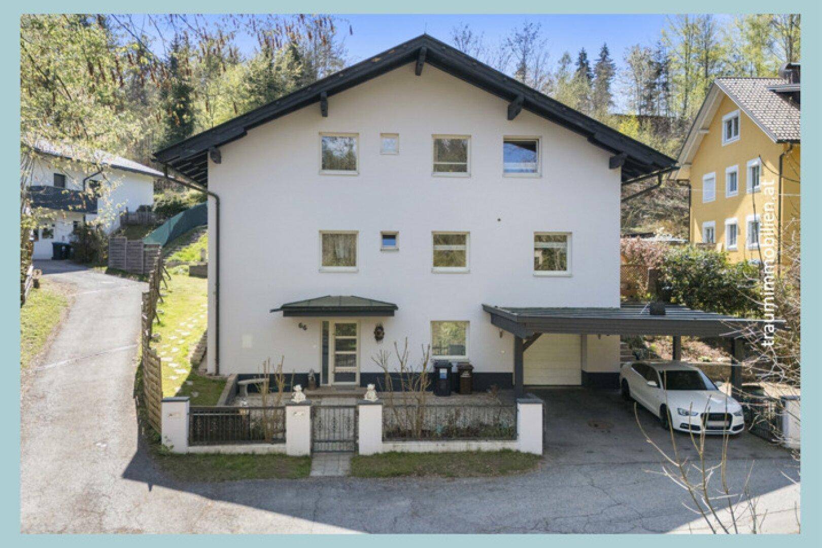 Modernes Einfamilienhaus mit weißer Fassade, Carport und gepflegtem Vorgarten.