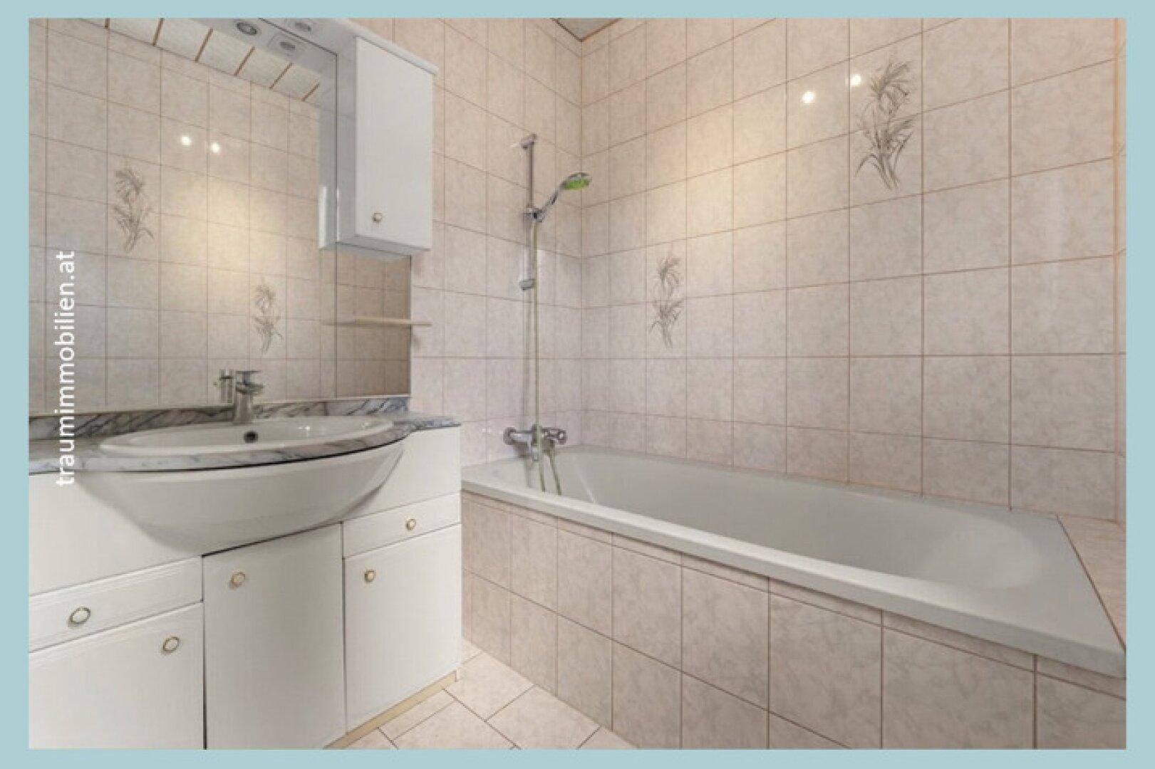 Badezimmer mit Badewanne, Waschbecken und hellen Fliesen an den Wänden.