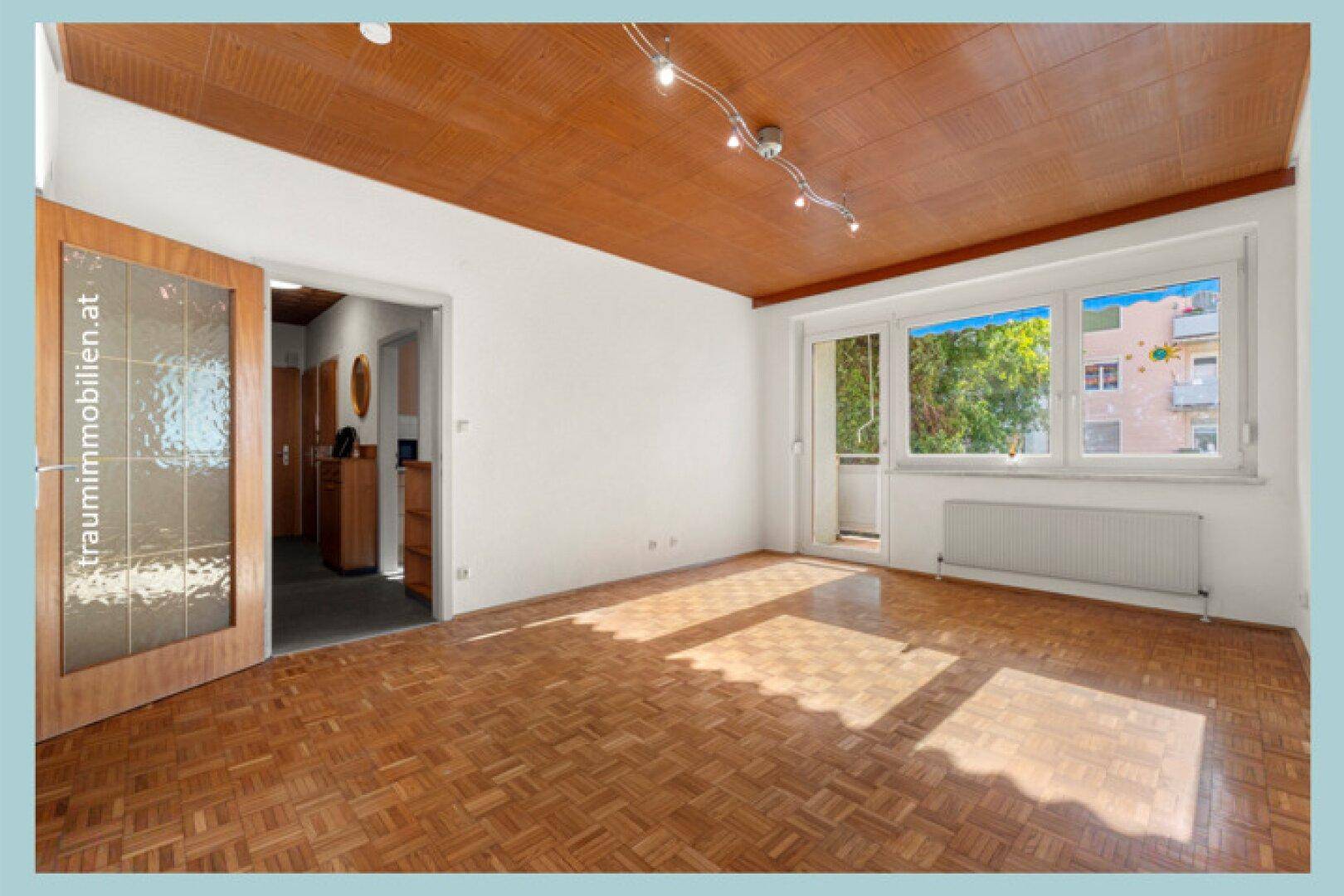 Helles Wohnzimmer mit Parkettboden, großem Fenster und Zugang zum Balkon.