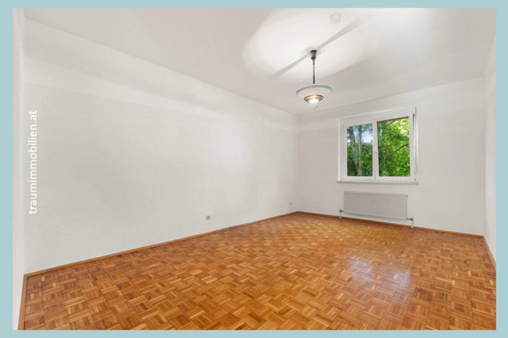Geräumiges Schlafzimmer mit Parkettboden, weiß gestrichenen Wänden und Fenster.